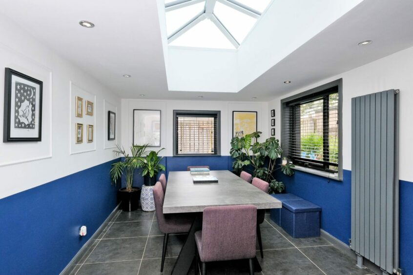 The dining room in the quirky aberdeen home has white and blue walls, black floor tiles, a concrete style table, six dining chairs and a skylight above the table