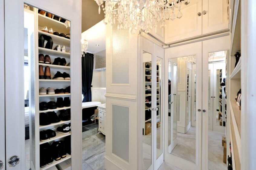 The walk-in wardrobe in the quirky aberdeen home with white cabinets and shelves and a crystal chandelier