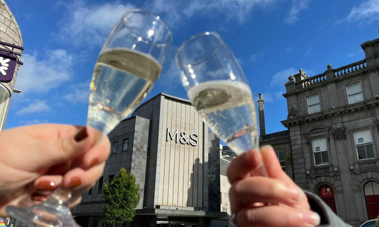 People clinking glasses of alcohol outside Aberdeen's M&S