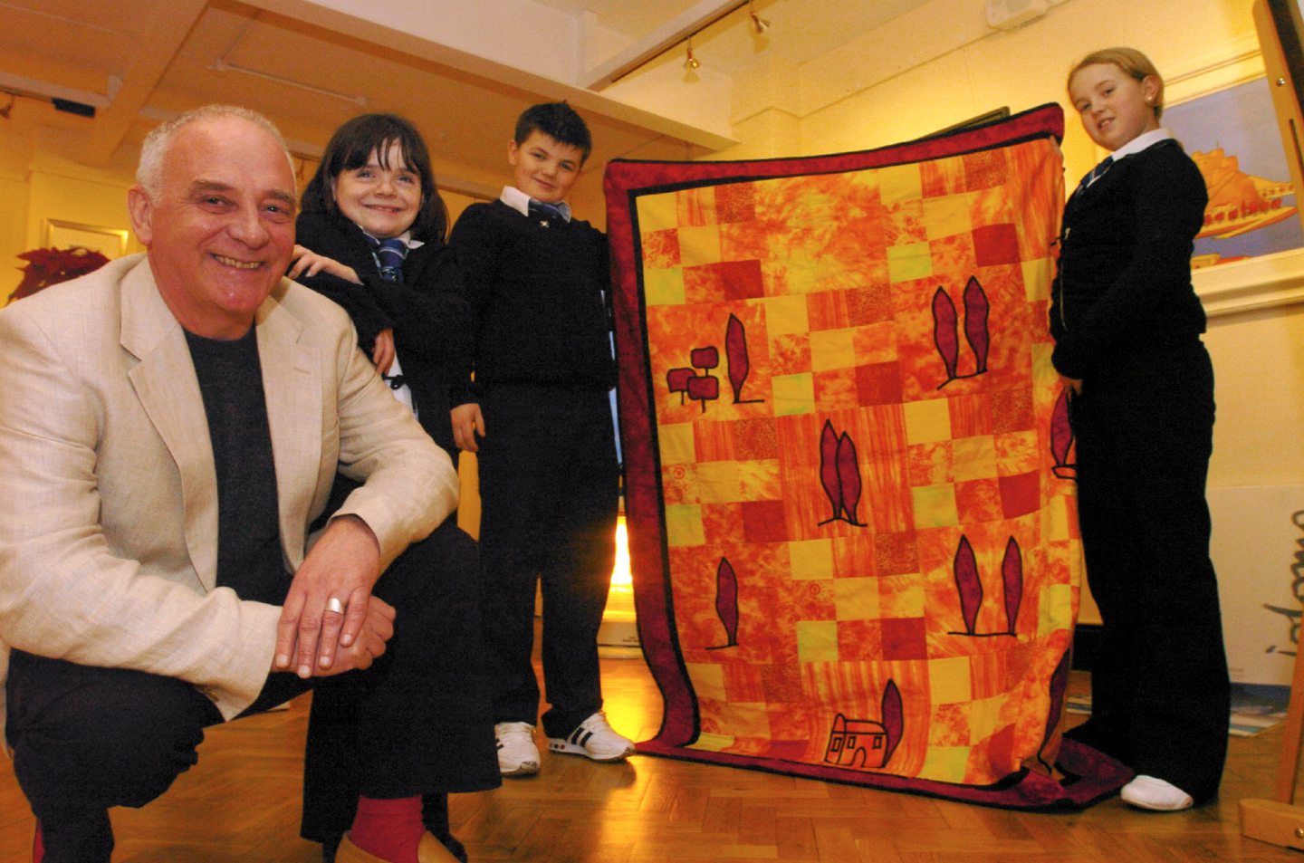 Iain Carby with kids from Walker Road School at his art Gallery and the quilt pupils made.