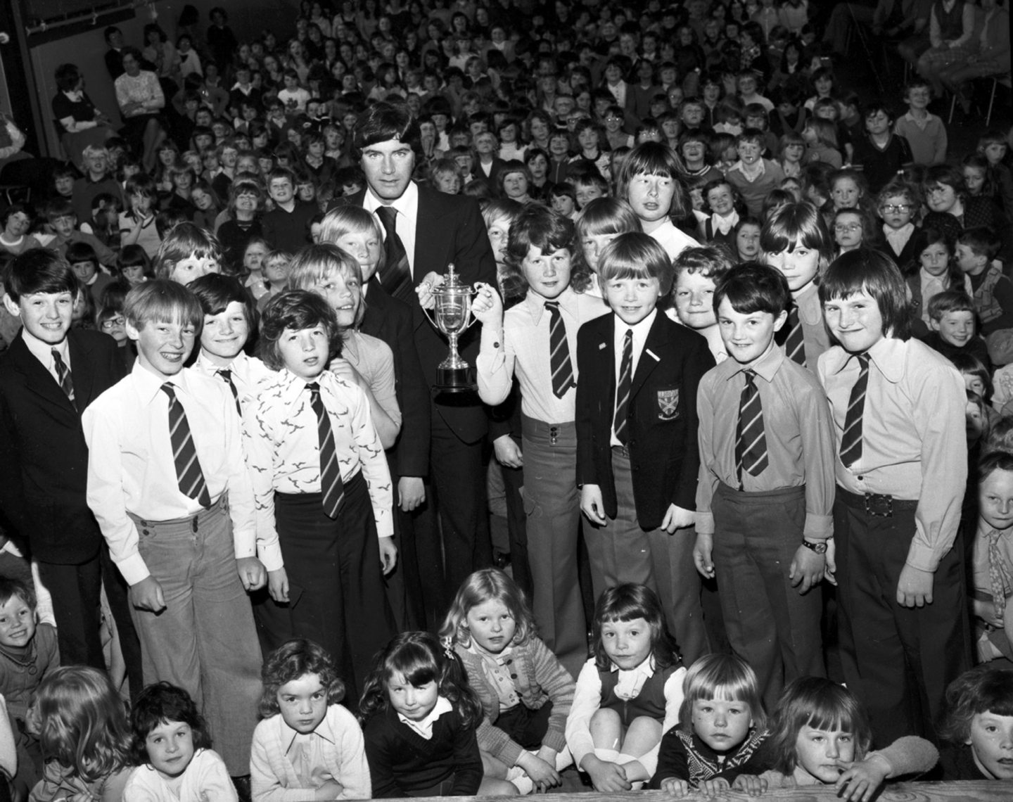 Manchester United captain and former Dons skipper Martin Buchan presenting the Aberdeen Primary League II trophy to Ronald Gray, captain of Walker Road's football team, at a special ceremony in the school hall in 1976.