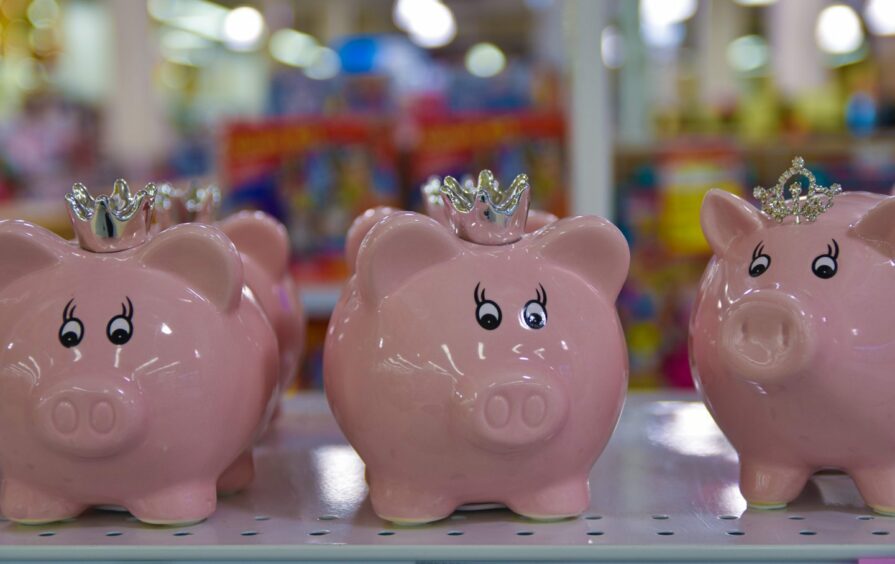 Three little piggy banks sit on the shelf of a store, looking worried