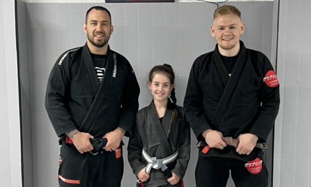 Pictures are three people in martial arts uniforms. Niamh Ross (centre) is one of Mikeysline's new Bee the Change champions. She is pictured here with SBG Moray coaches Martin Donaldson (left) and Kevin McAloon. Image: Mikeysline. Picture shows; Niamh Ross (centre) is one of Mikeysline?s new Bee the Change Champions. She is pictured here with SBG Moray coaches Martin Donaldson (left) and Kevin McAloon.