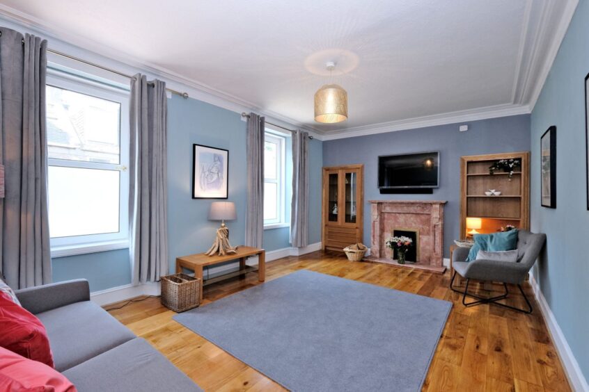 A living area in the Ferryhill home with blue walls, wooden floors, two bookcases, a fireplace and a grey sofa and chair.