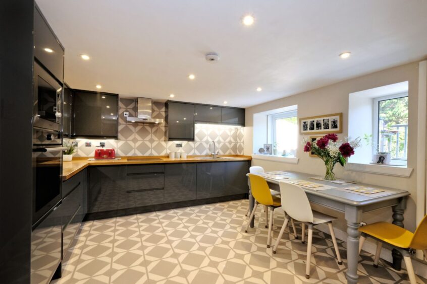 The kitchen of the Ferryhill home with black cupboards with yellow countertops, grey and white floor tiles and a dining table with four chairs