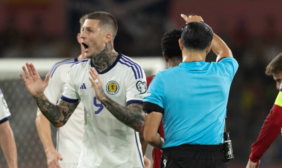 Scotland's Lyndon Dykes is shocked by the referee Serdar Gozubuyuk awarding him a yellow card.