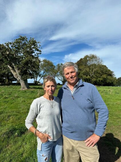 Edward with wife Charlotte standing in a field with trees and blue sky.