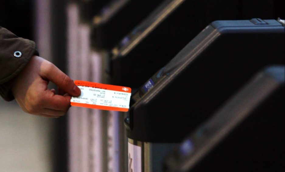 Commuter inserting ticket into ticket barrier at railway station.