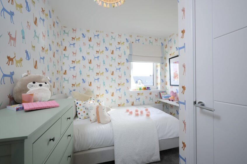 The children's bedroom with white bedsheets, a pale green dresser and colourful cat wallpaper