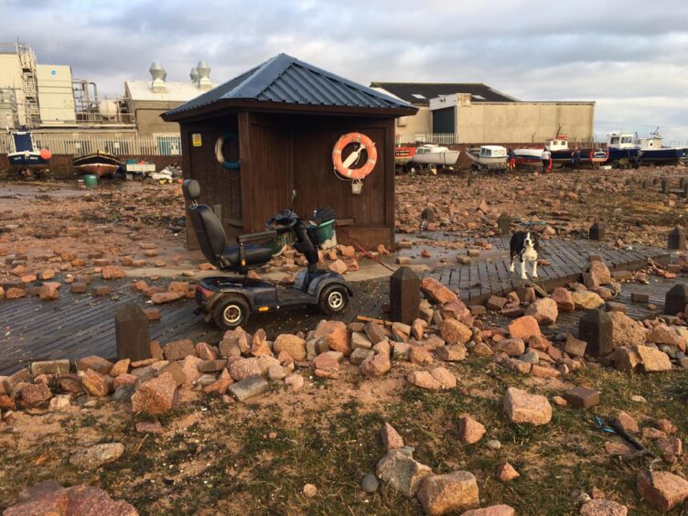 Damage at Boddam Harbour, with mobility scooter stopped and dog standing.