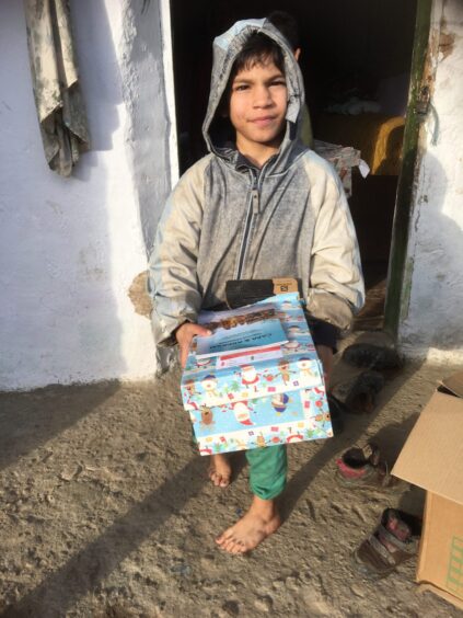 barefoot boy wearing a hoodie holds a gift-wrapped shoebox