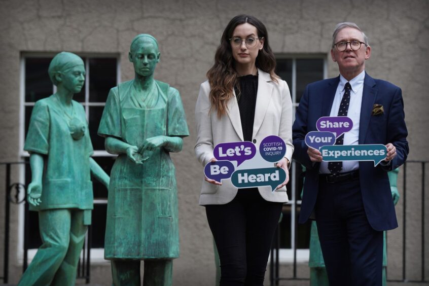 a woman and a man hold signs urging everyone to take part in the Scottish Covid-19 inquiry's Let's Be Heard listening project