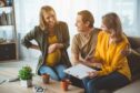 Pregnant woman looks at piece of paper held by smiling future parents with law on surrogacy in the UK possibly set to change