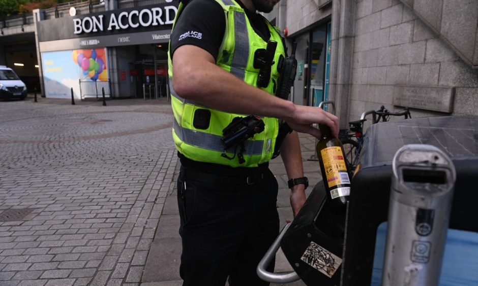 A police officer putting a bottle of Buckfast alcohol in the bin in Aberdeen.
