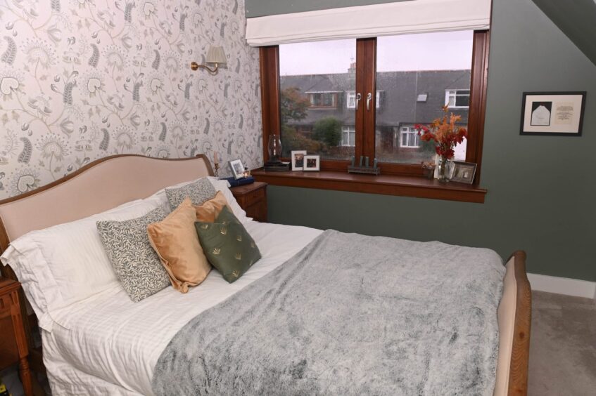 A bedroom in the period property in Aberdeen, with dark wood accents, sage green walls, a floral feature wall and a cosy double bed