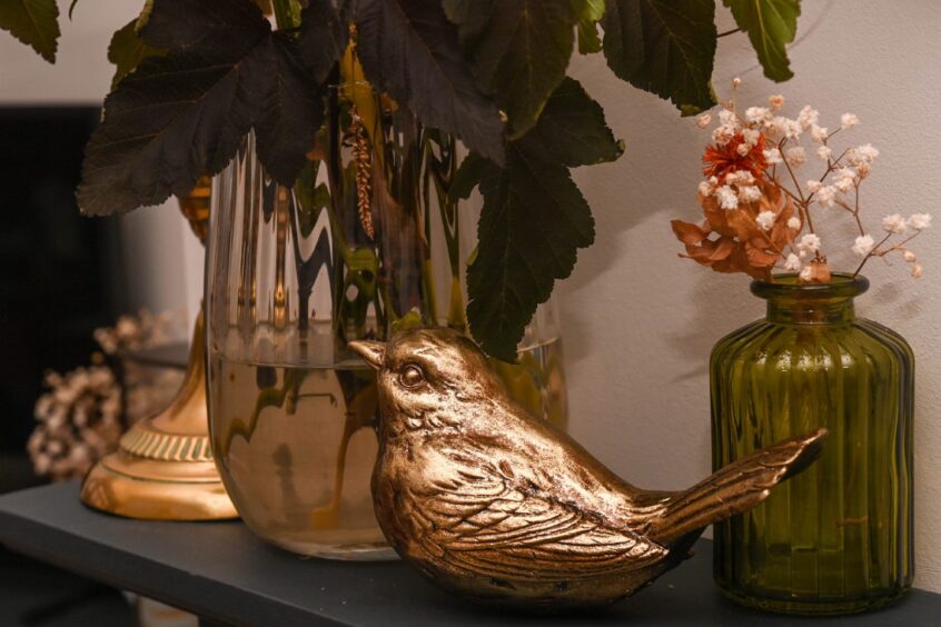 An golden bird ornament next to a small vase of dried flowers and a large vase of fresh flowers
