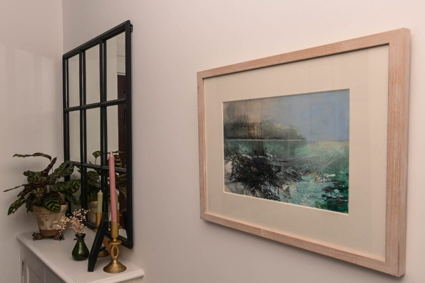 a painting on the wall next to a mirror and a shelf with houseplants and candlesticks