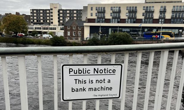 A white public notice sign attached to the railings on Ness Bridge in Inverness, which reads: "This is not a bank machine."