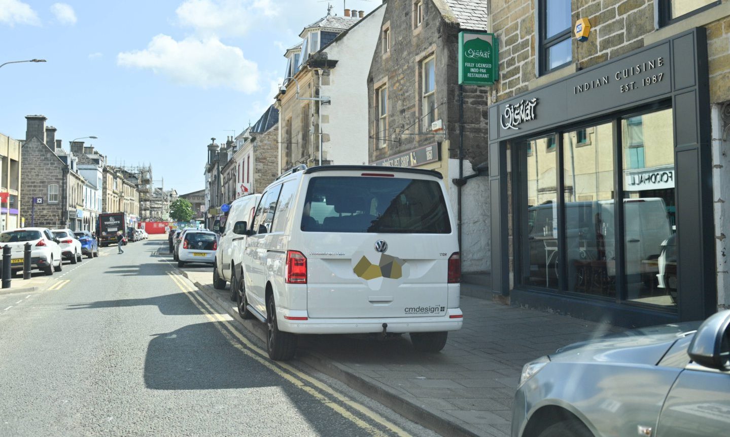 Multiple cars parked on pavement on Elgin High Street.