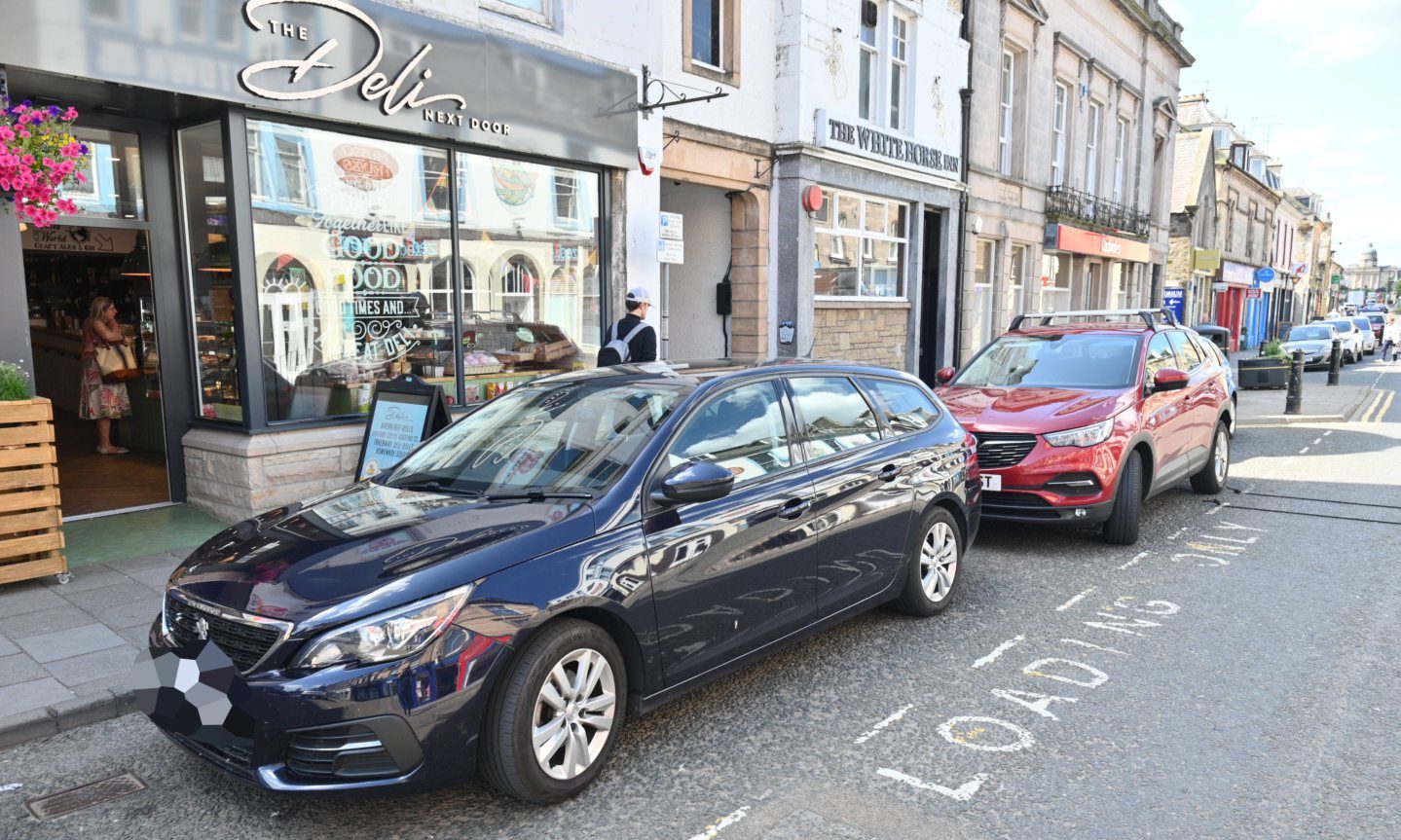 Two cars parked in loading bays on Elgin High Street. 