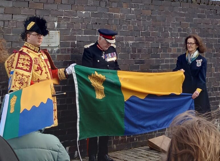 Lyon Court honorary vexillologist Philip Tibbetts unveiling the new Moray flag with the county's Lord Lieutenant Seymour Monro and Vice-Lieutenant Nancy Robson. 