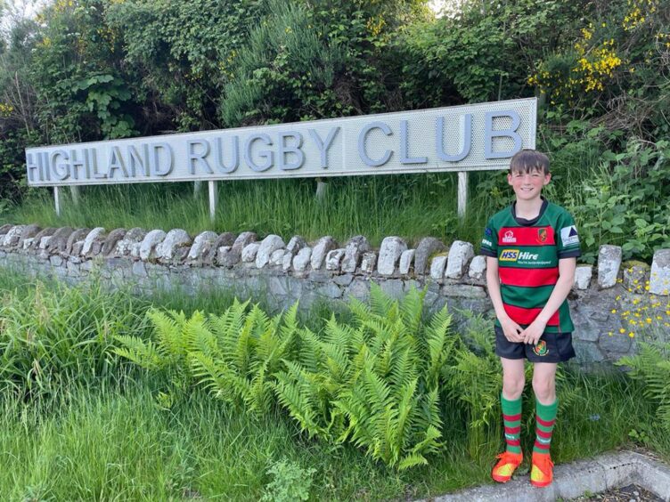 Alastair Grant pictured by the Highland Rugby Club sign dressed in his red and green strip.