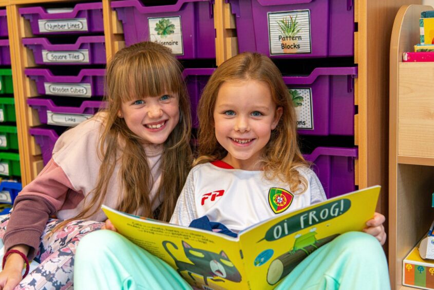 Two young ISA students reading a book in their school classroom.
