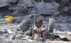 A Palestinian boy sits on the rubble of his building destroyed in an apparent Israeli airstrike in Nuseirat camp in the central Gaza Strip. Image: AP Photo/Hatem Moussa