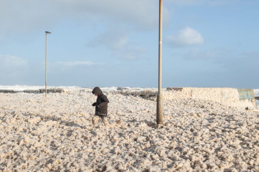 Young boy plays in the seafoam at Lossiemouth.