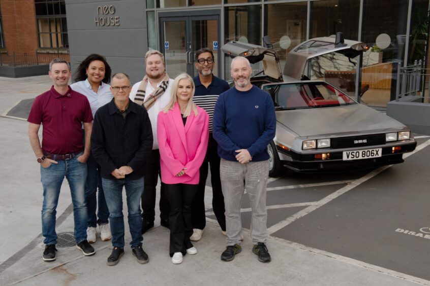 The panellists standing next to a DMC DeLorean car.