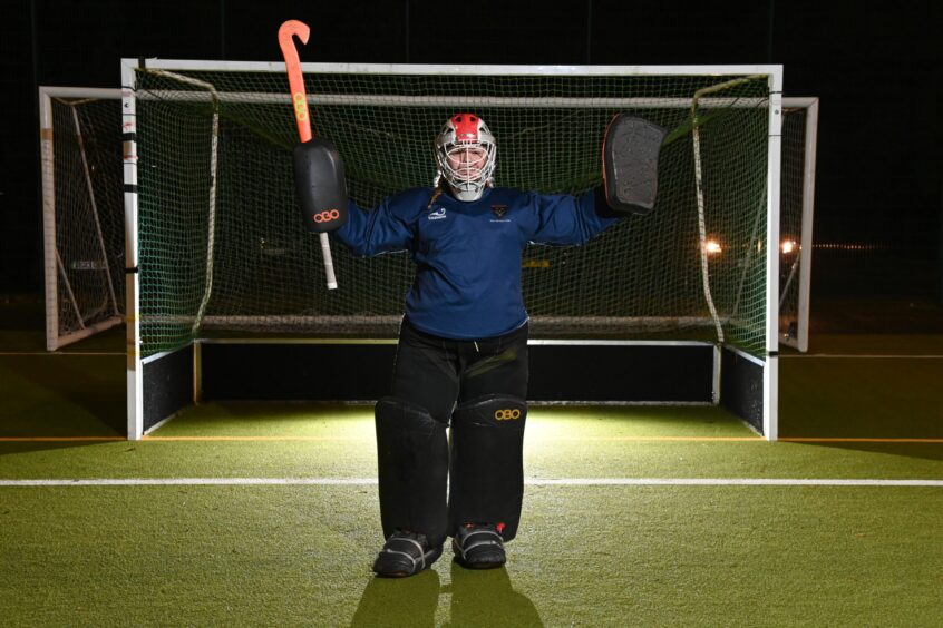 Ellon Hockey Club goalie Keira Hochifelden stands in front of her goal with arms spread wide.