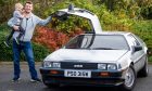 John McAulay holding son Fraser in one hand with other on top of popped open door of DeLorean.