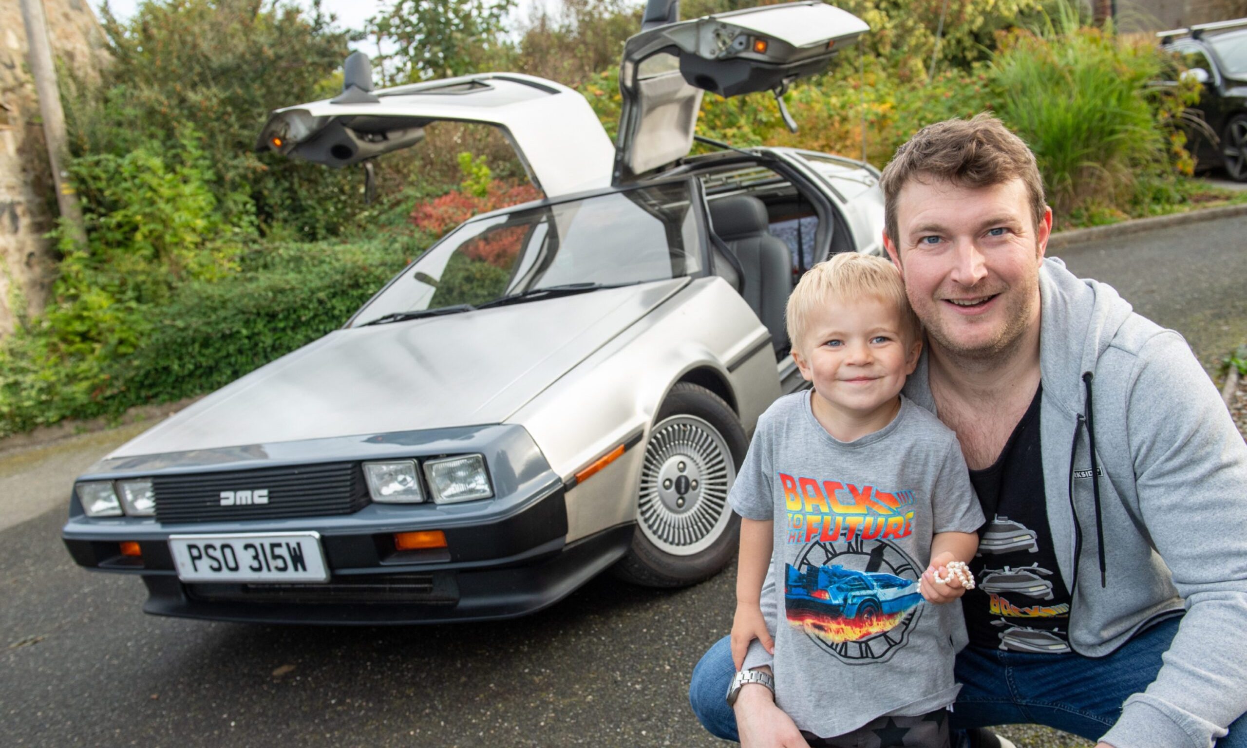 John McAulay and son Fraser wearing Back to the Future t-shirts with DeLorean behind. 