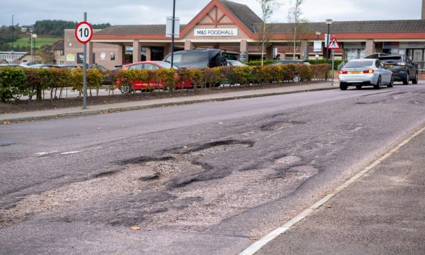 Westhill Shopping Centre car park entrance. Potholes and car on the road.