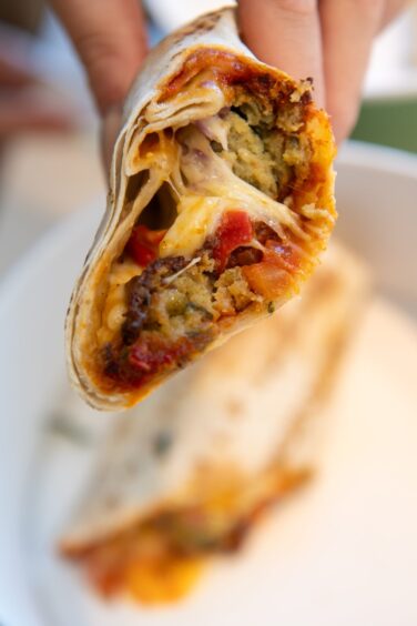 View of the fillings inside the wrap, featuring halloumi, falafel, diced red onion, chargrilled red peppers and more.