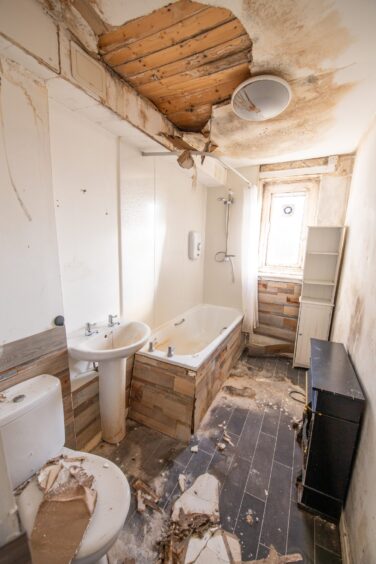 The bathroom, with the debris from the ceiling across the floor, toilet, sink and bath