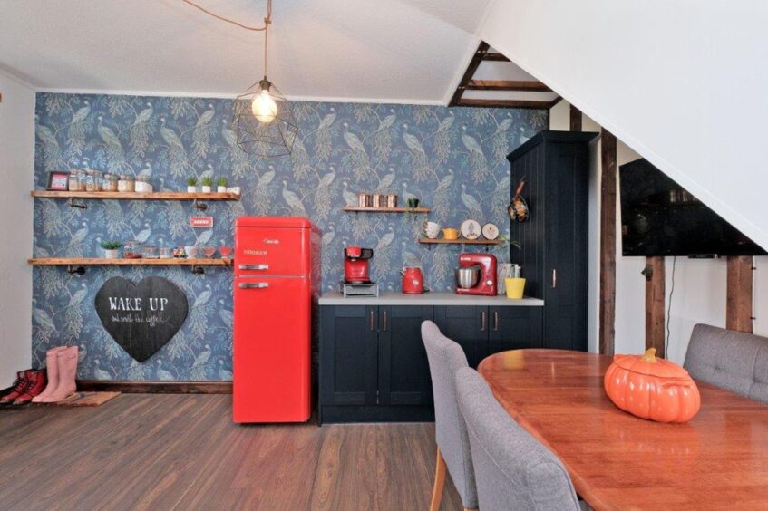The kitchen in the bridge of don home, with red appliances, a wooden dining table, grey dining chairs and black cabinets