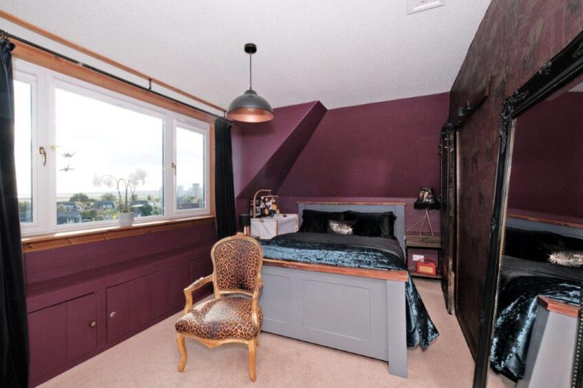 The bedroom has purple walls, a large floor length mirror, a bed with velvet sheets and a leopard print chair