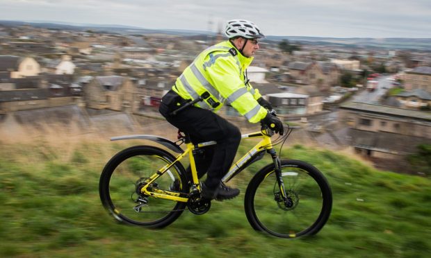 Side-on view of police cyclist with view over Elgin rooftops behind.