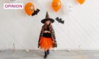 A girl dressed as a witch with Halloween decorations behind her