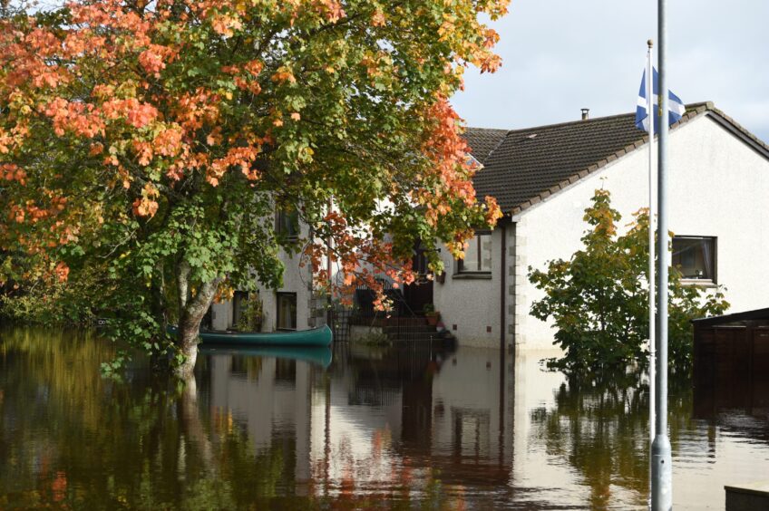 Flood water surrounds a white home in Aviemore as the trees bloom with autumn colours.