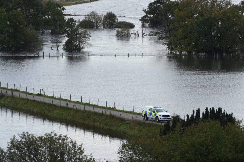 A vehicles drives along a road as fields on both sides are covered in flood water.