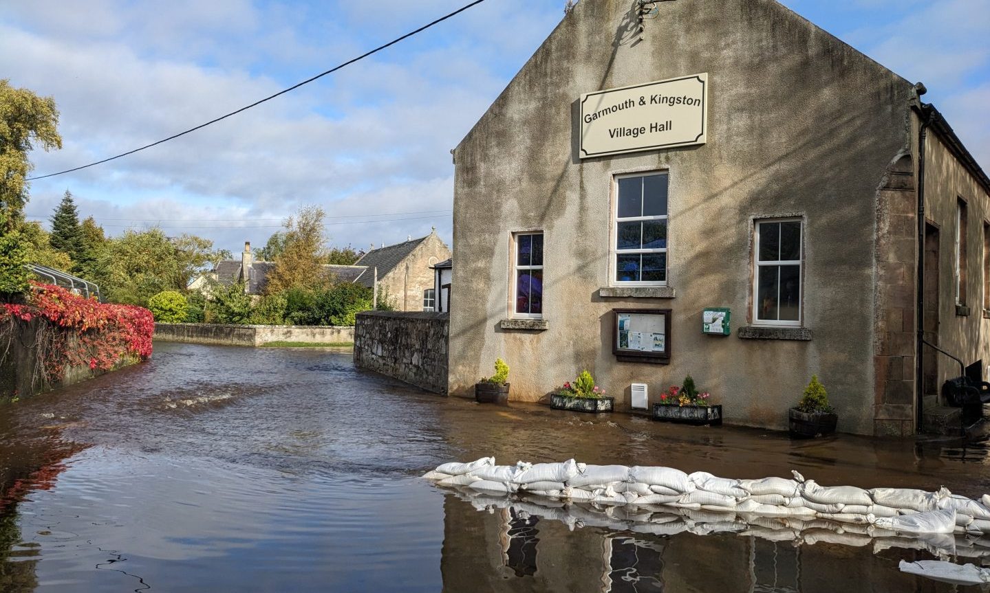 Garmouth Village Hall surrounded by water with sandbags in foreground. 
