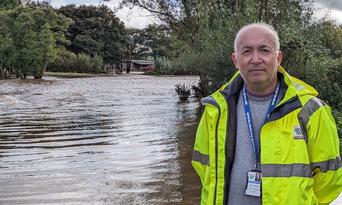 Marc Macrae wearing high-viz yellow jacket with flood water behind. 