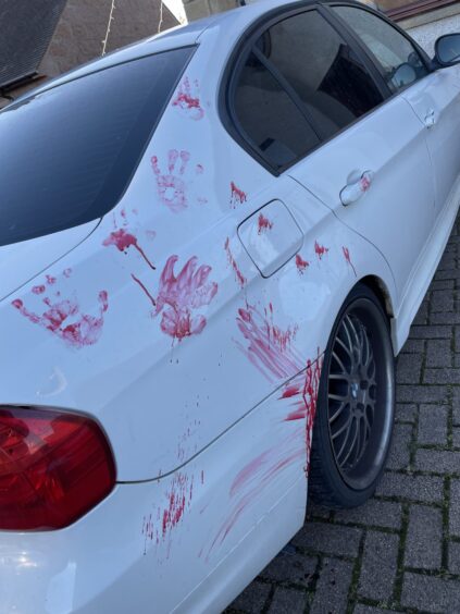 White car covered in red painted handprints.