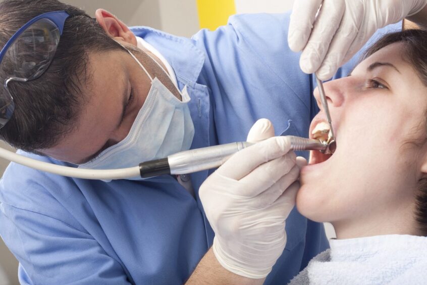 A dentists inserts a drill into a patients mouth.