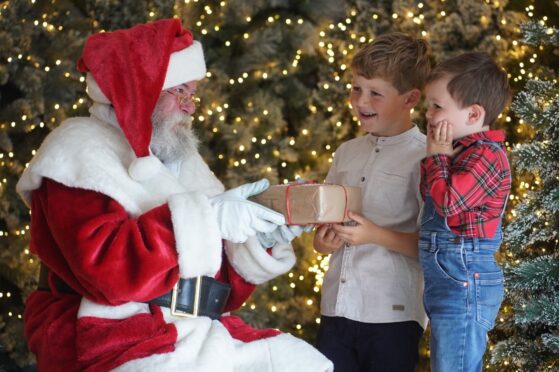 Santa hands gifts to two boys at a Christmas grotto in a Dobbies garden centre.
