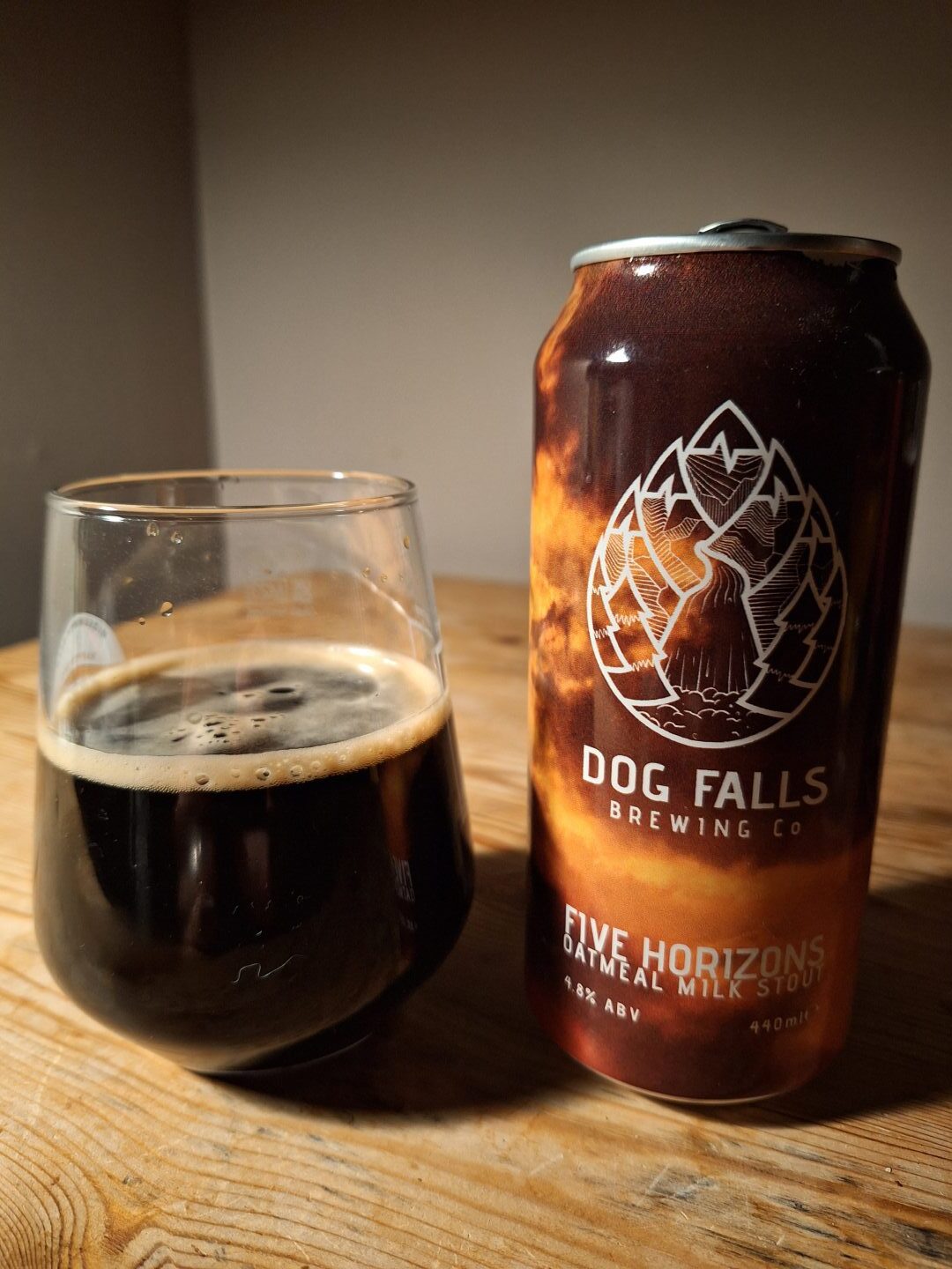 A dark Dog Falls stout beer inside a glass, next to a can from the Inverness brewery. 