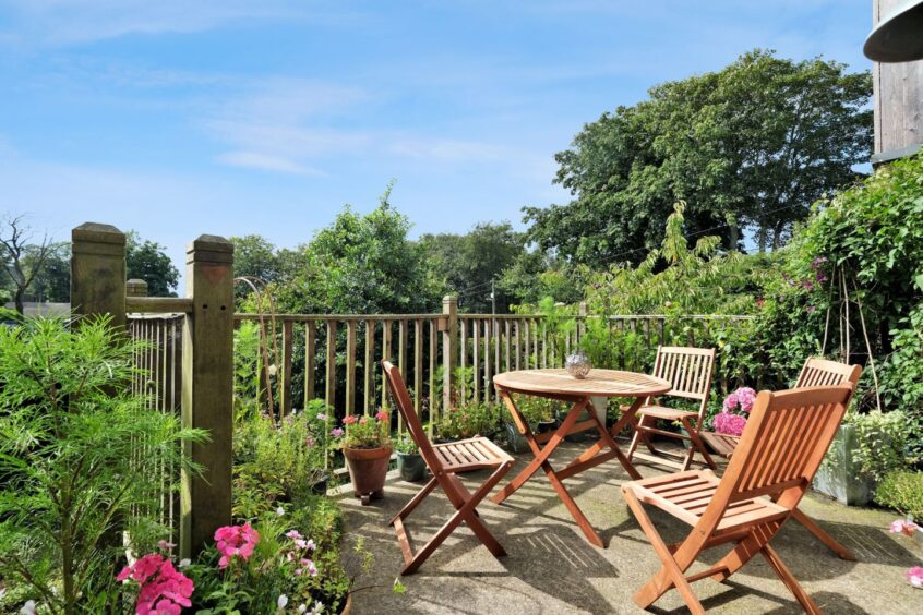 A seating area in the garden of the inverurie home after the renovation, there is a round wooden table with four wooden folding chairs surrounded by greenery