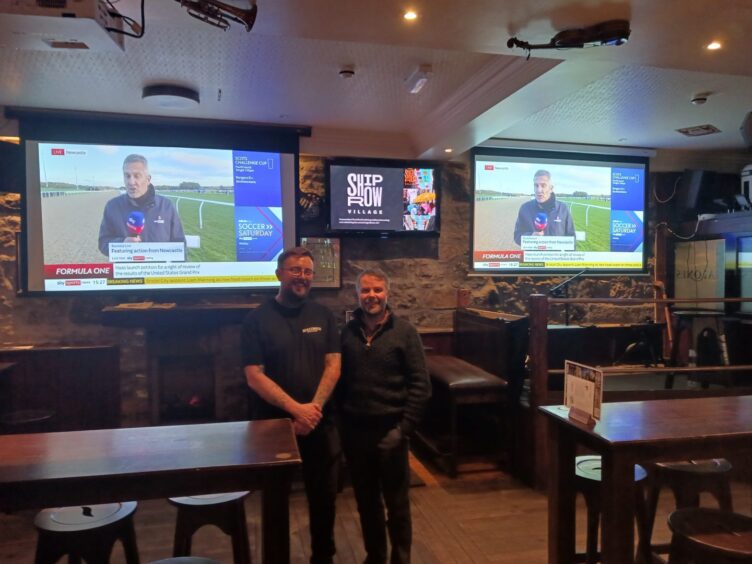 Two men standing in front of big screens.